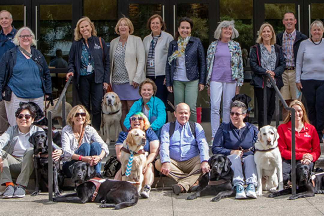 A large group of people and guide dogs pose for a group photo.