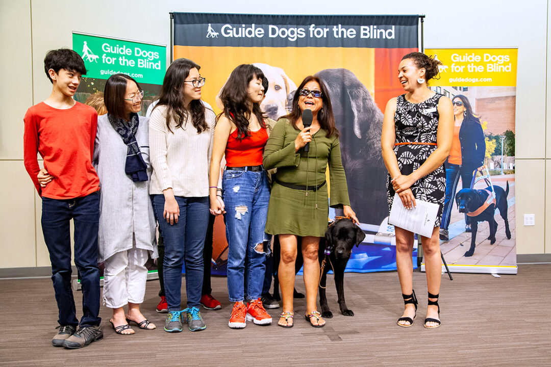 A family of volunteer puppy raisers, a woman with a guide dog, and a guide dog mobility instructor at a GDB graduation ceremony.
