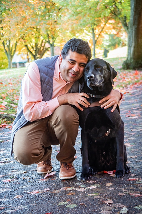 Amit Ahuja crouching next to his black Lab guide dog, Tashi.