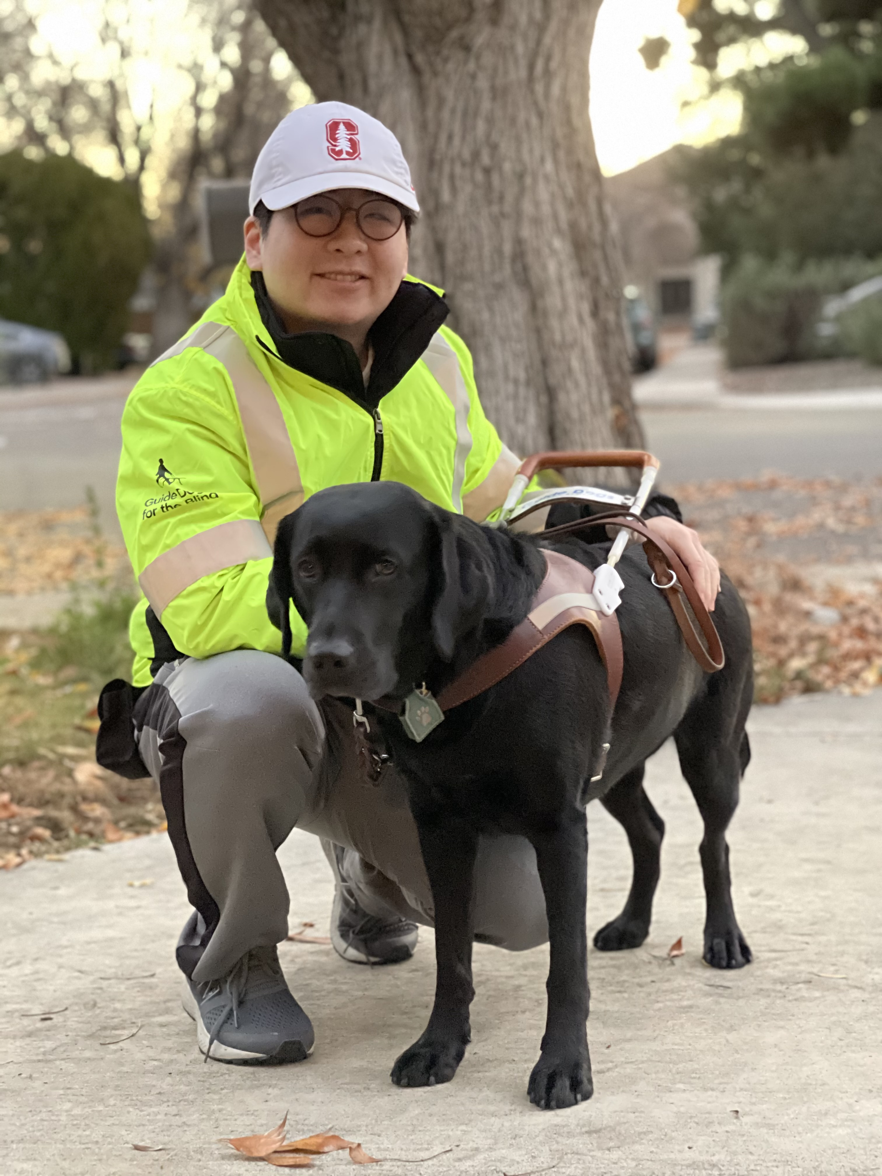 A man kneels next to a black Lab guide dog.