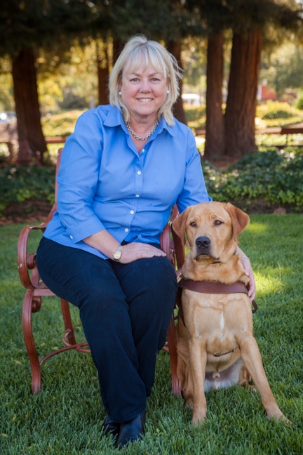 A portrait of Joan Boyd sitting next to a yellow Lab guide dog.