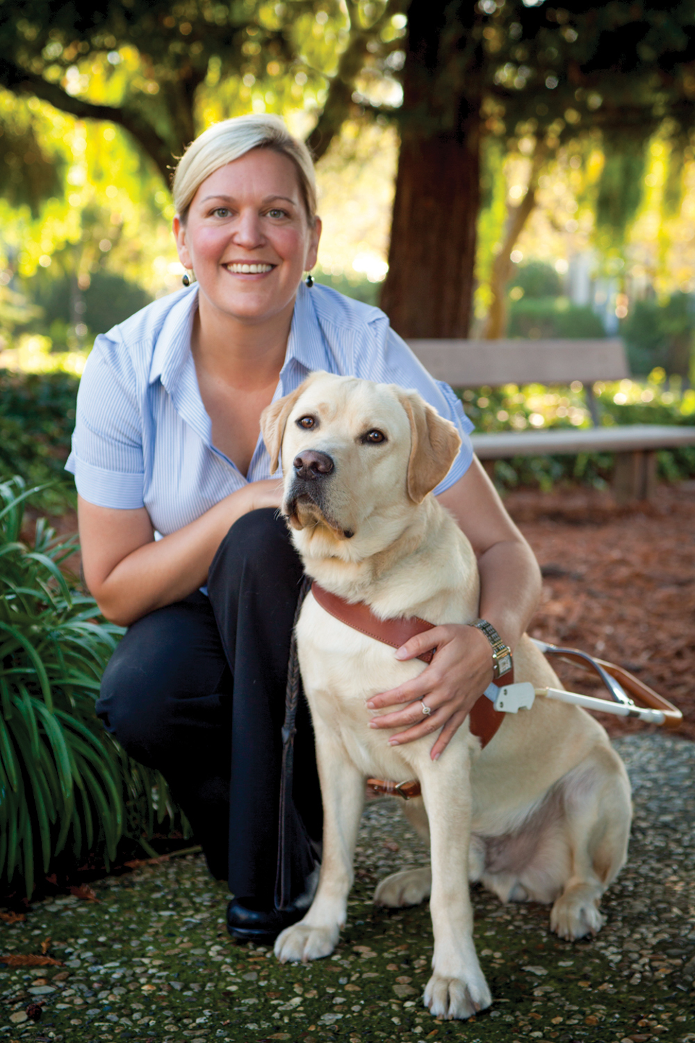 A portrait of Susan Armstrong sitting next to a yellow Lab guide dog.