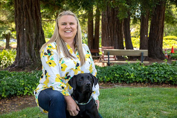 Erin Jones kneels next to a black Lab dog.