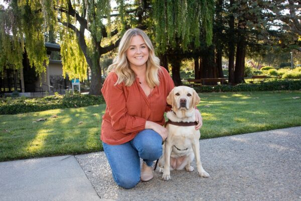 Jillian Fish kneeling next to a yellow Lab guide dog.