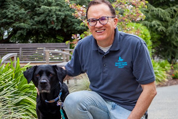 Marty Scherstuhl kneels next to a black Lab