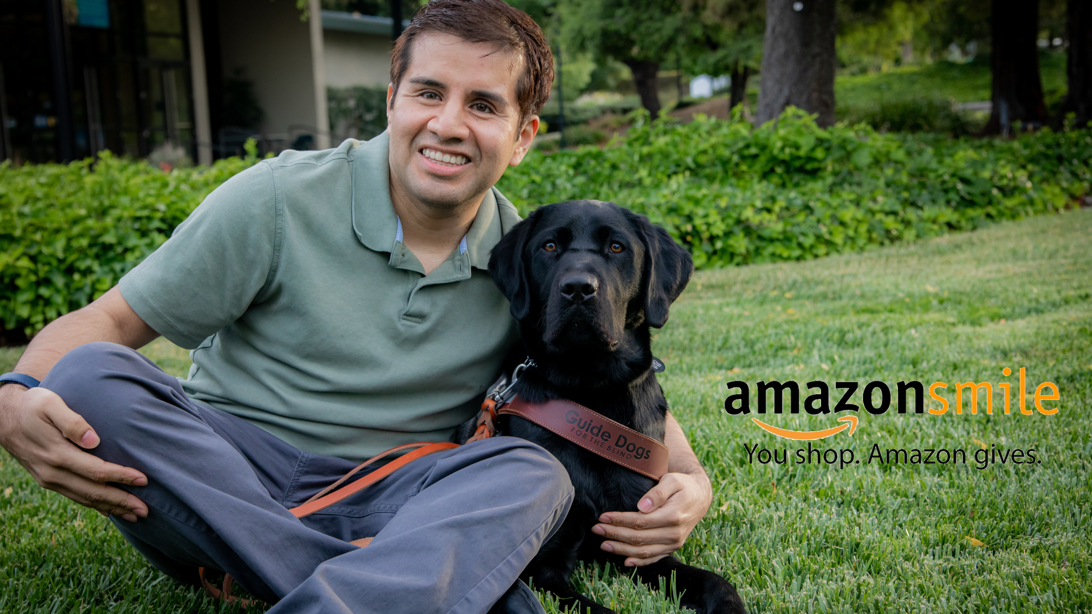 Belo Cipriani is seated on the grass beside his black Lab guide dog, Limo. The AmazonSmile logo appears to the right.