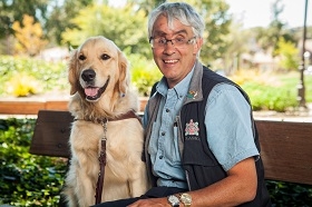 GDB grad Bruce Gilmour sits on a bench with his golden retriever guide dog Marley