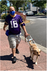 Dimitrios walks down a street with his guide dog Cami