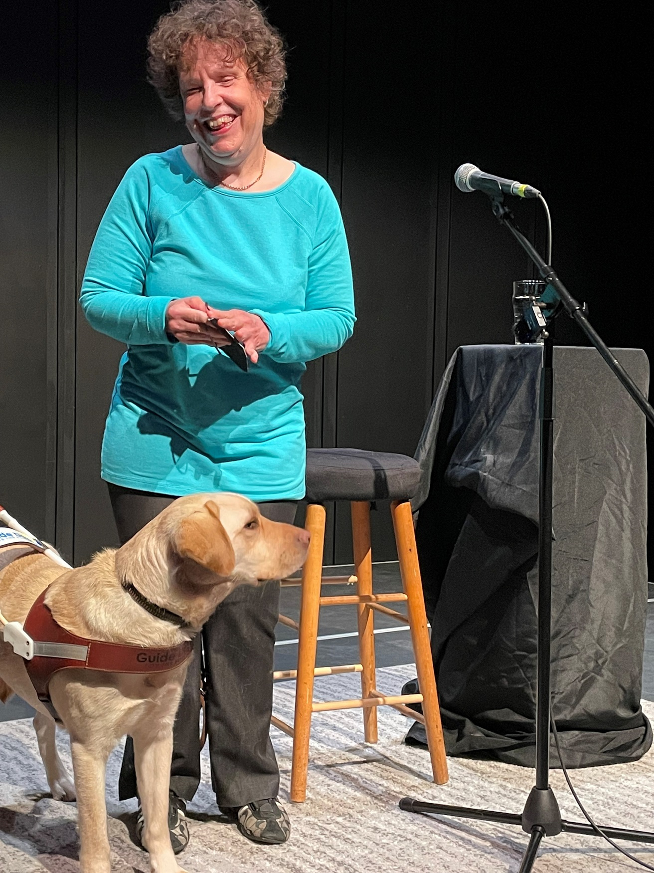 Kim stands on stage smiling with her yellow lab guide dog.