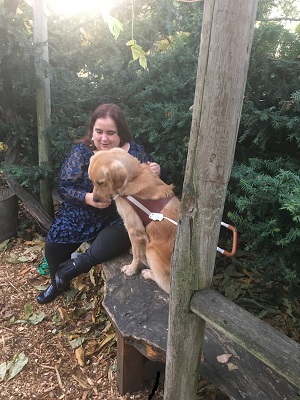 Maia Scott and her guide dog Gleam sit on a bench in the woods