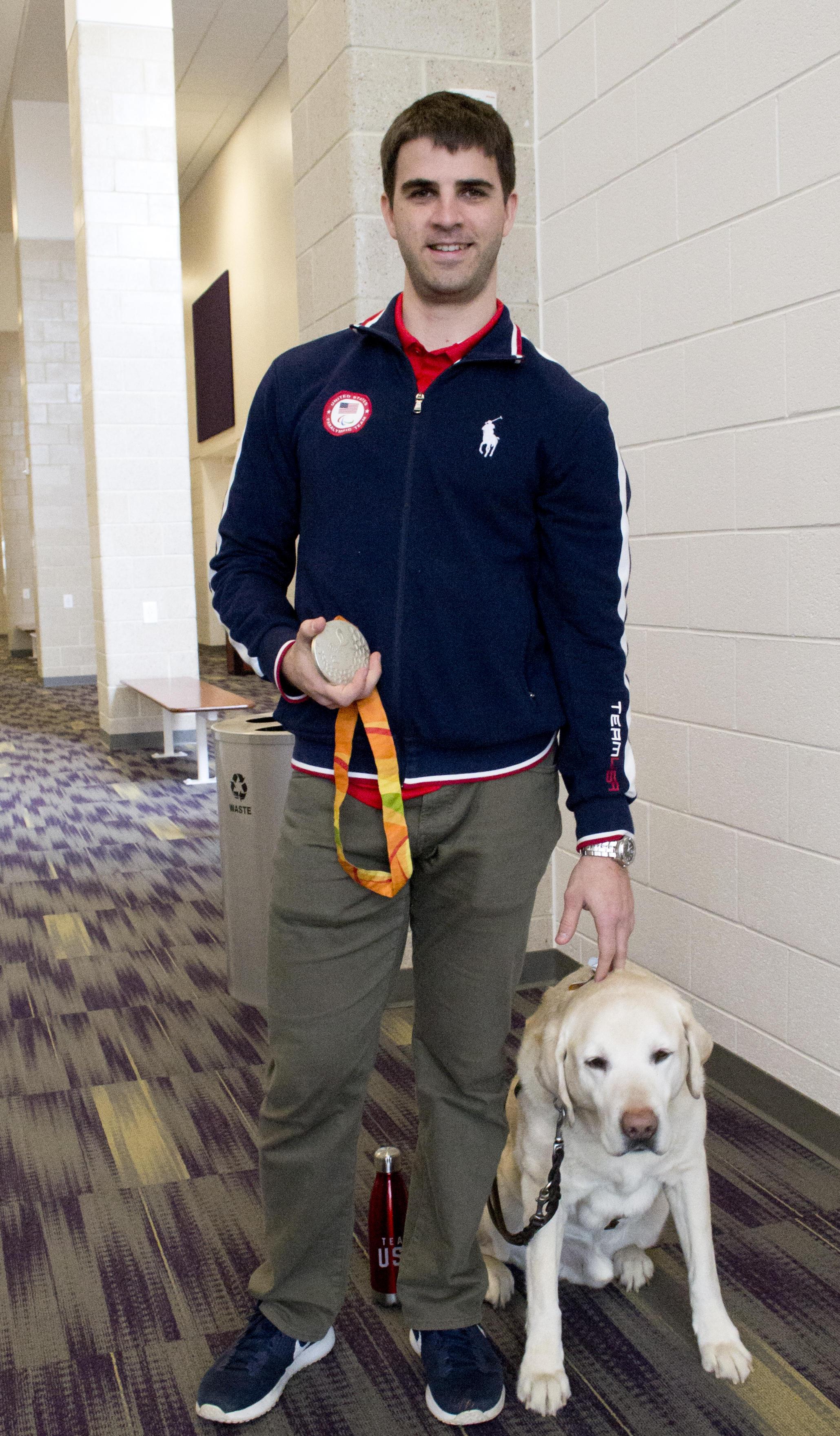 Paralympian Matt Simpson poses with his silver medal and his yellow Lab guide dog, Lacrosse.