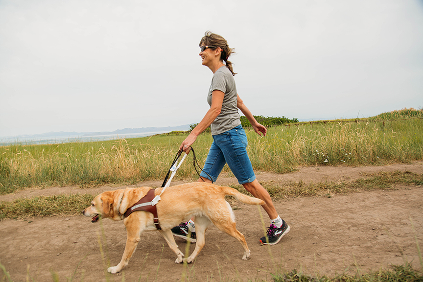 Becky and her guide dog Georgie quickly walking along a hiking path.