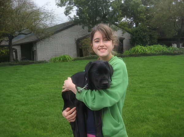 A young woman holds a black puppy in her arms.