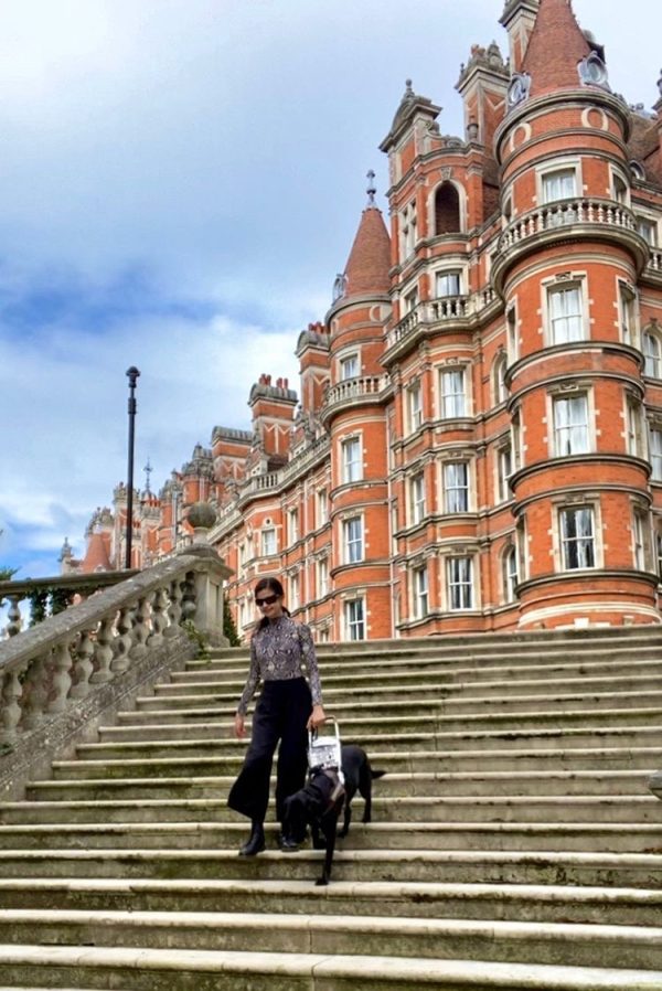 GDB Grad Aria Mia Loberti and black Lab guide dog Ingrid descend the stairs at Royal Holloway University
