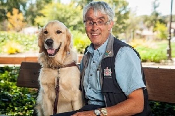 GDB grad Bruce Gilmour sits on a bench with his golden retriever guide dog Marley