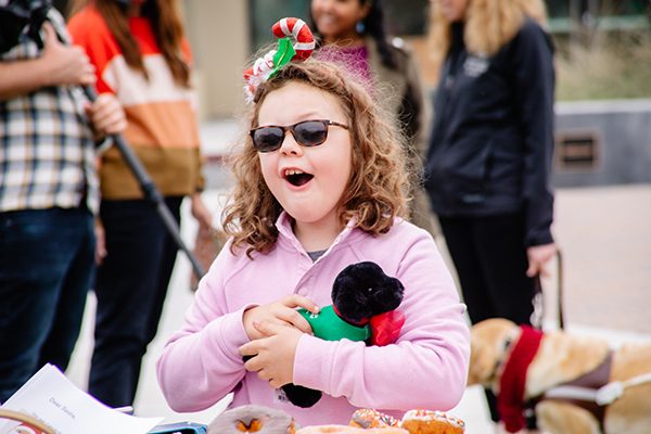 A beaming young girl wearing festive holiday attire holds a plush puppy.