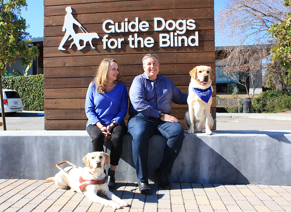 Elizabeth Gard and Tom Furlong sit in the GDB courtyard flanked by two yellow Labs.