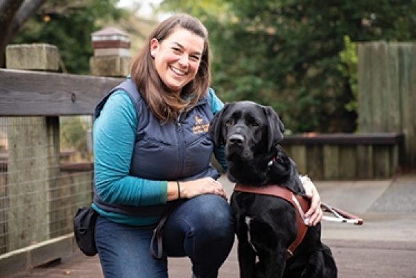 Guide Dog Mobility Instructor Gina Paolini with a black Lab guide dog in harness.