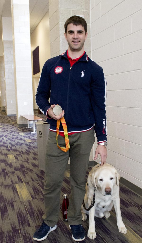 Paralympian Matt Simpson poses with his silver medal and his yellow Lab guide dog, Lacrosse.