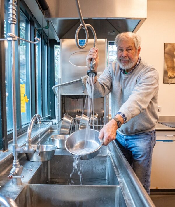 A person washes dog dishes in a large commercial sink.