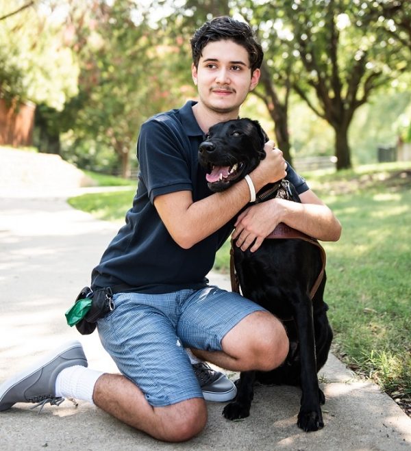 GDB Grad Zack Thibodeau kneels beside black Lab guide dog Namath in the park.