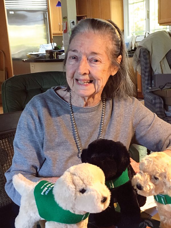 Leslys Garrow Vedder smiles holding three plush guide dogs in green training vests.