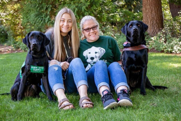 Two teen girls pose for a portrait with two black Labs.