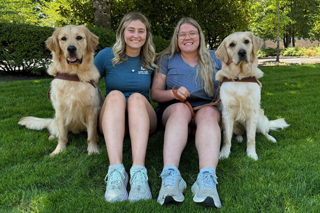 Two young women pose for a portrait with two Golden Retrievers.