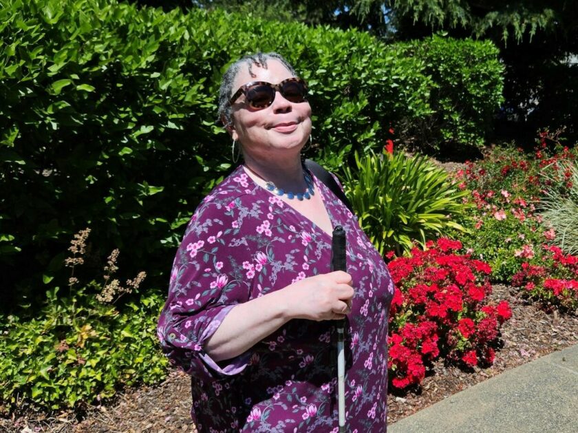 A woman stands confidently holding her white cane.
