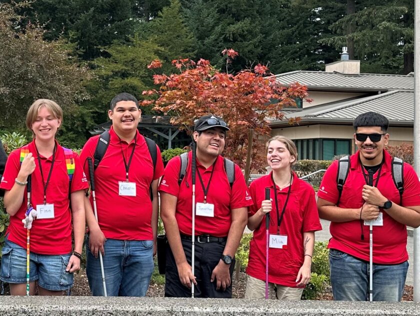 A group of young adults in matching red t-shirts stand smiling with their canes