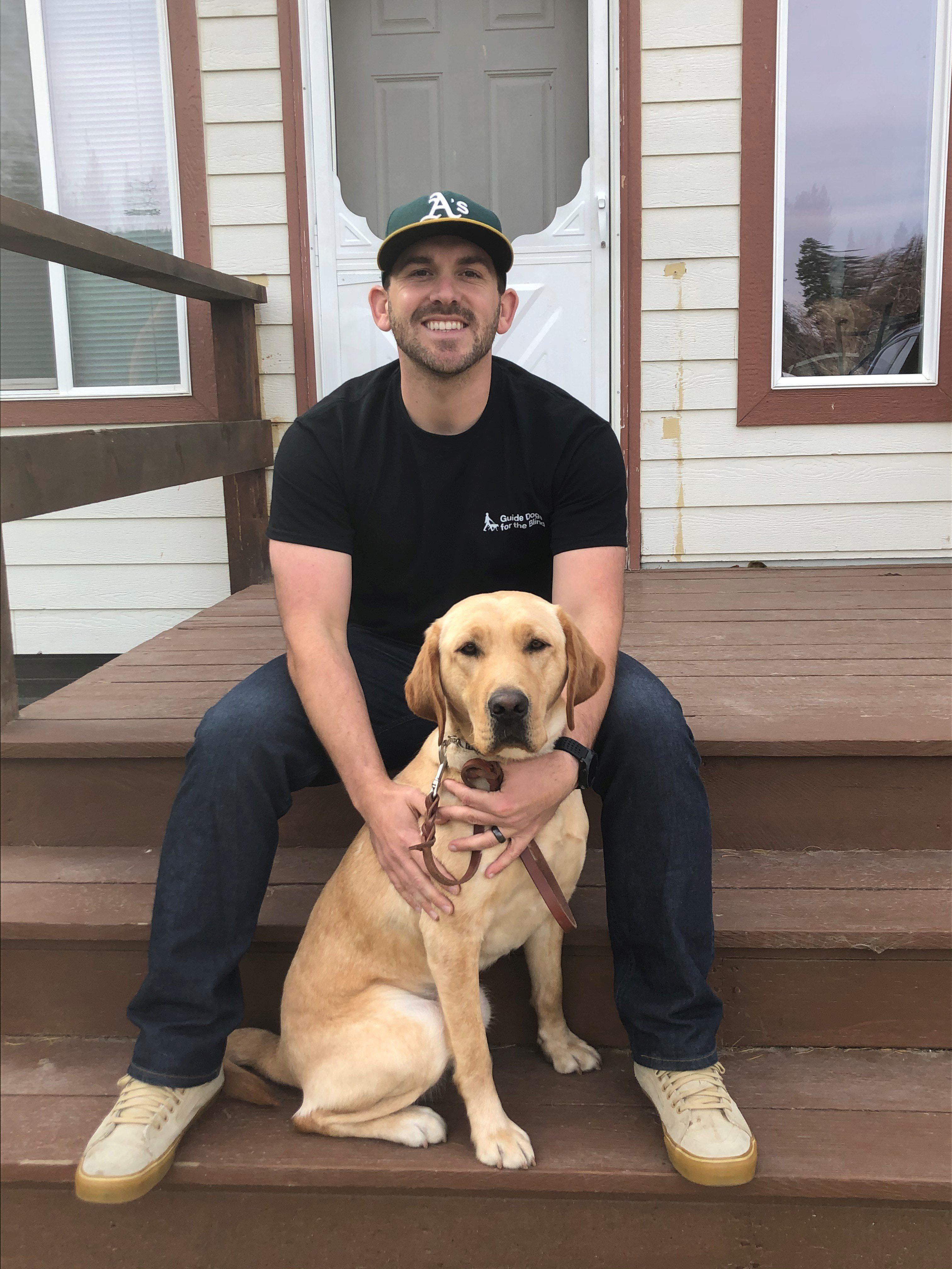 GDB Instructor Adam Gilbert is seated on the steps of a home with a yellow Lab guide dog during an in-home training.