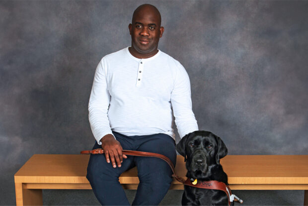 GDB client seated on a bench with a black Lab guide dog by his side.