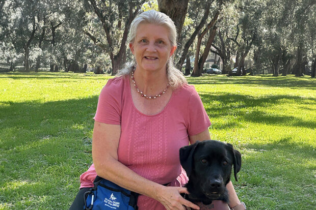 GDB client kneels beside a black Lab guide dog in a park setting.