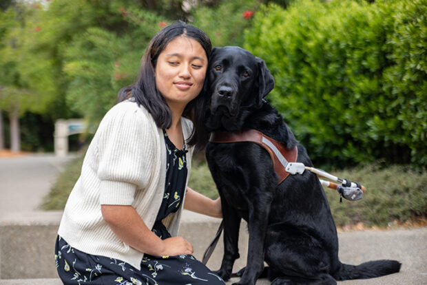 A client sits cheek-to-cheek with their black Lab guide dog.