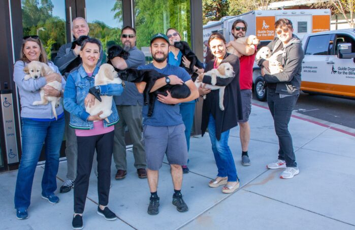 GDB staff stand together in front of the puppy truck. Each person holds a cuddly puppy in their arms