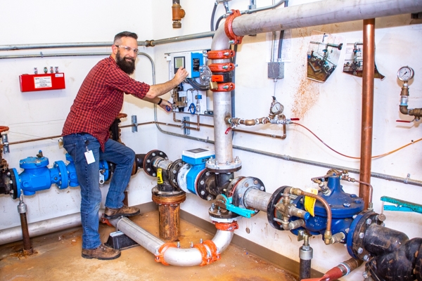 A man working on pipes inside of a large boiler control room.