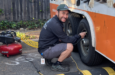 A man inspects and services a tire on a multi-wheel trailer.