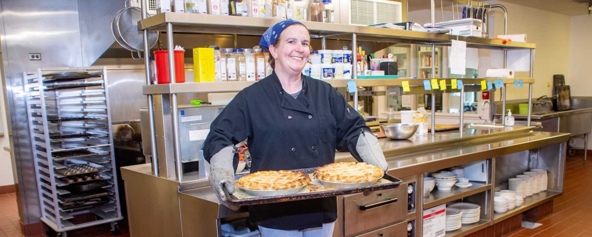One of the GDB chefs in teh GDB kitchen, posing with two freshly-baked pies that she has just pulled from the oven.