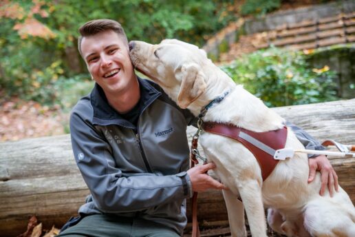 A portrait of Joey and a yellow Lab guide dog in a wooded area.