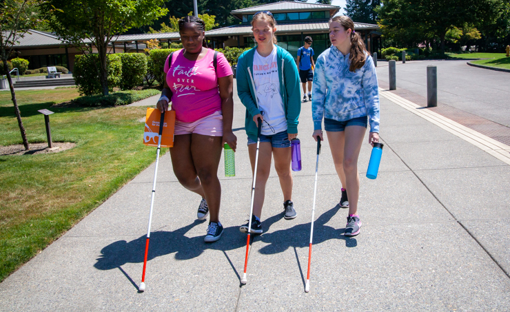 Three young adults walk together using their white canes.
