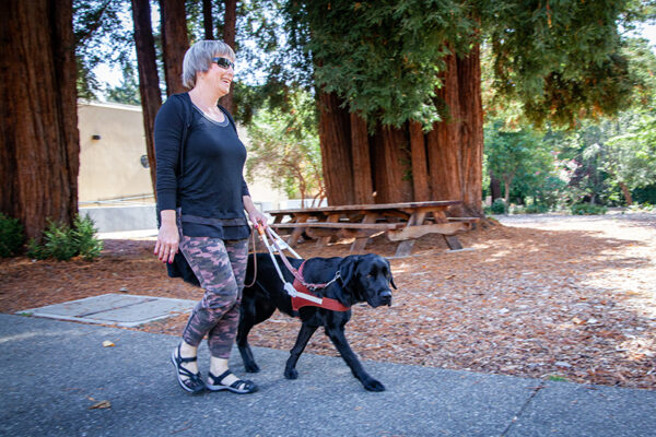 A woman walks along a wooded path with her guide dog.