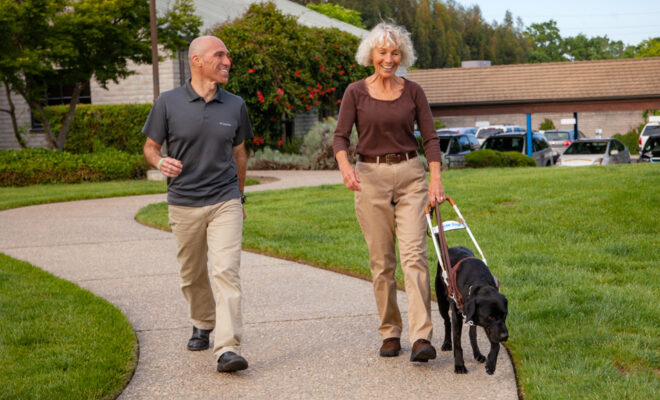 A guide dog mobility instructor walks on a path with a client and her new guide dog on GDB's California campus.