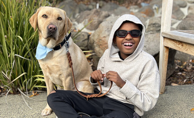 A boy sits next to his yellow Lab K9 Buddy dog.