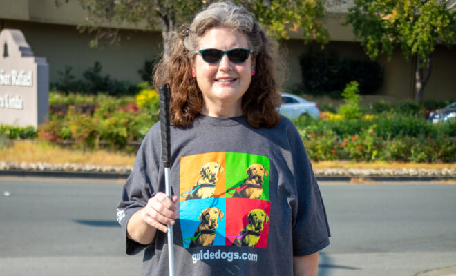 A smiling woman holds a white cane.