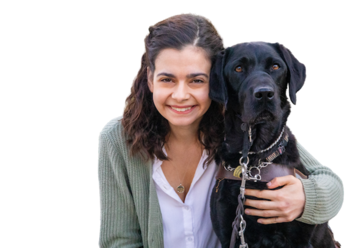 Aria smiles into the camera with her arm around her black Lab guide dog's shoulders.