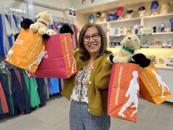 GDB Volunteer Laura holds up arms full of gift bags in the California Gift Shop.