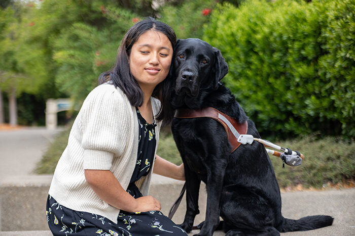 A Guide Dogs for the Blind client poses with black Lab guide dog in a harness.