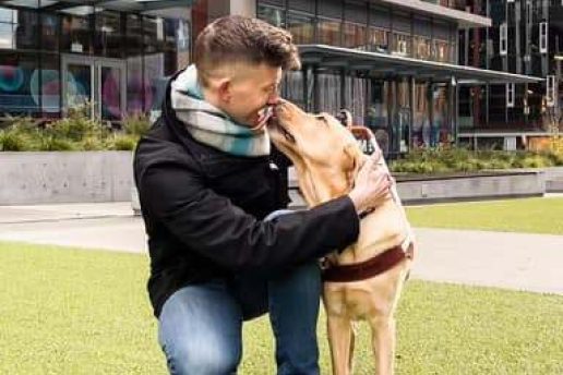 A man kneels next to his guide dog.