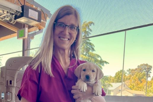 A smiling woman holds a puppy.