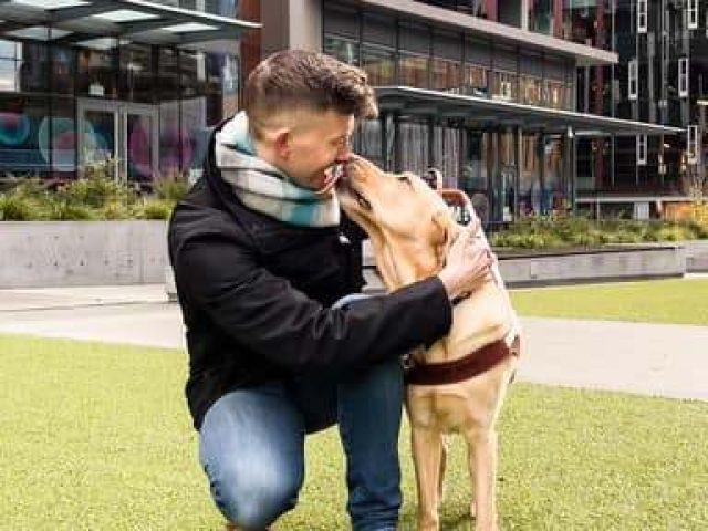 A man kneels next to his guide dog.